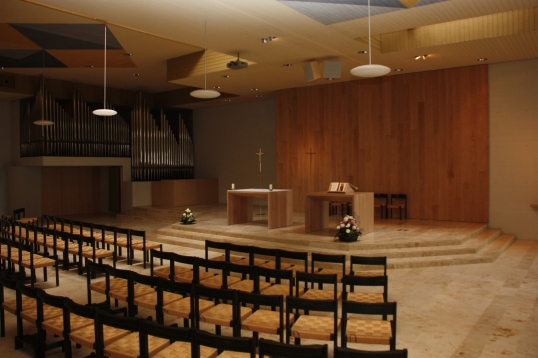 Church interior with seating, altar, wooden wall and organ pipes.