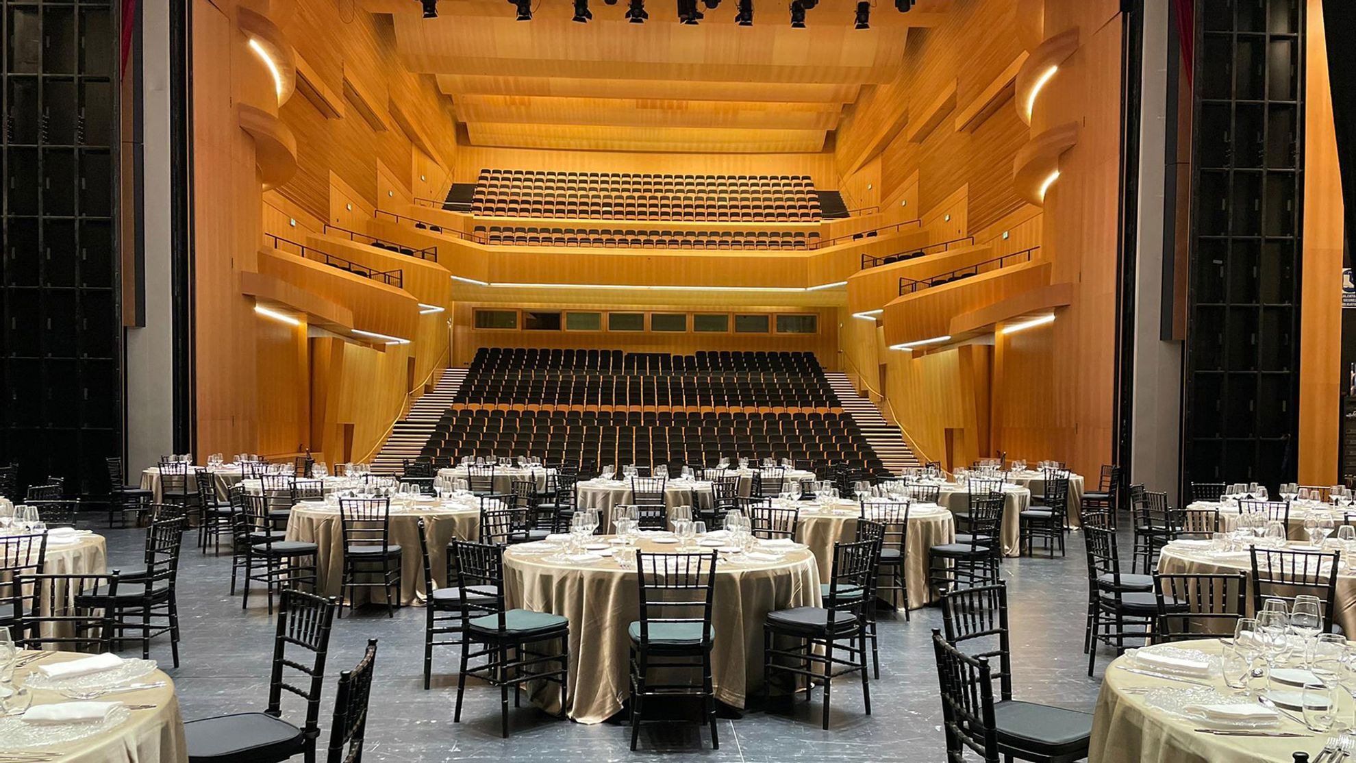Sala Teatro audience seating and balconies seen from stage; foreground banquet tables show a rental configuration.