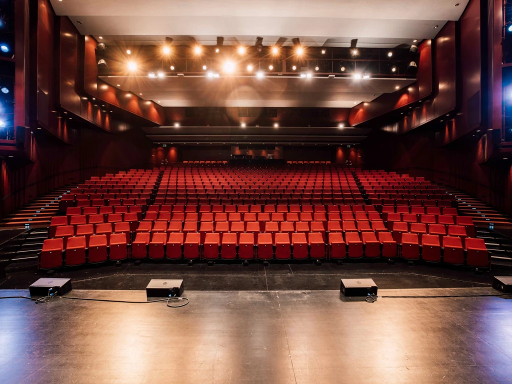Theatersaal red seating and dark balconies seen from stage.