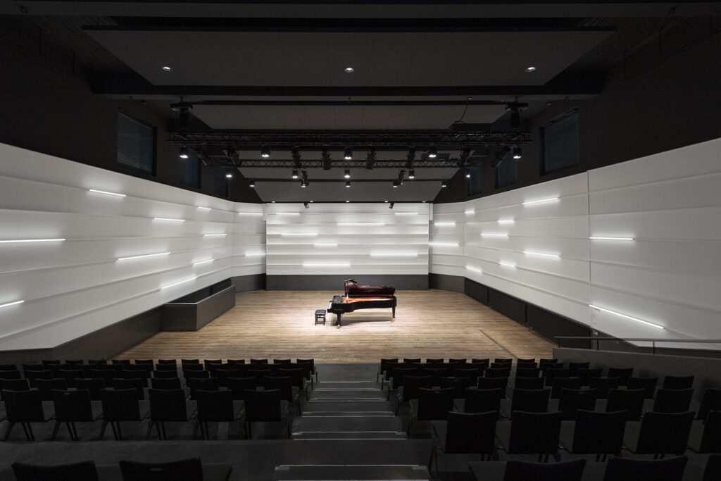 Concert hall with grand piano and audience seating.